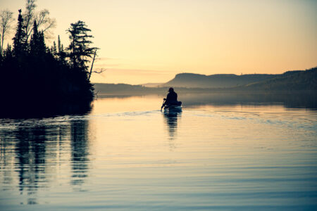 Silhouette of person paddling canoe on calm lake at golden sunset