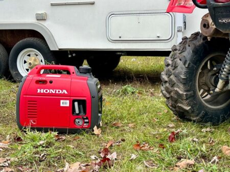 Red Honda portable inverter generator on grass beside RV and ATV tire.
