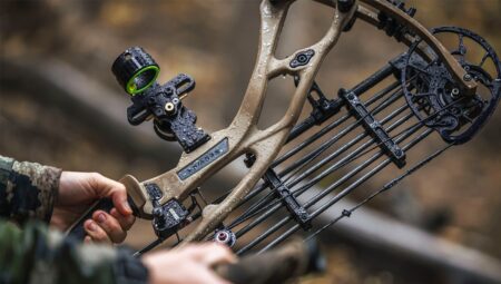 Wet compound bow held by hunter in camouflage during rainy outdoor hunting session