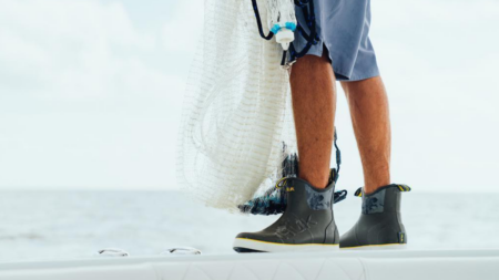The Best Fishing Shoes of 2024 Fisherman wearing HUK ankle boots holding a cast net on a boat deck