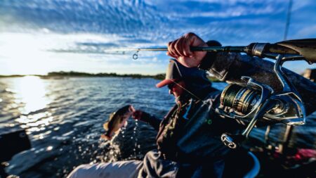 The Best New Reels at ICAST 2024 Angler reeling in a fish from a boat at sunset on calm waters