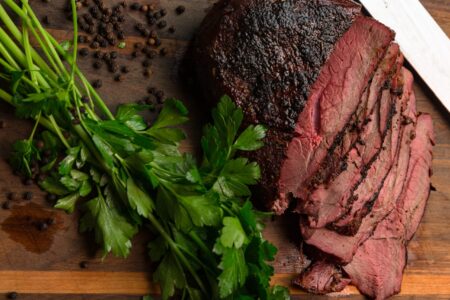 The Complete Guide to Butchering and Cooking Venison Roasts Sliced smoked beef brisket with dark crust on wooden cutting board with parsley