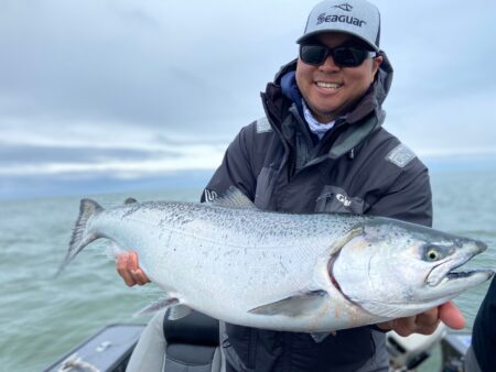 Man in Seaguar cap proudly holds large silver salmon on fishing boat