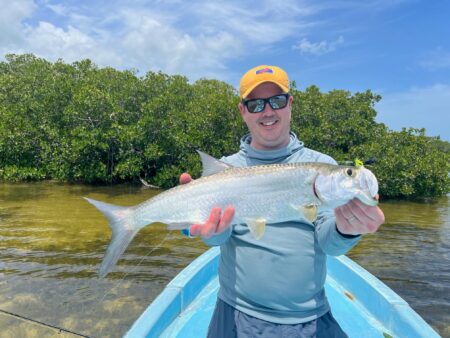 Man holding large silver tarpon fish while fishing near mangroves from blue boat.