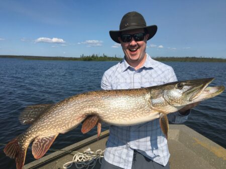 Smiling man holding large northern pike fish on boat in lake