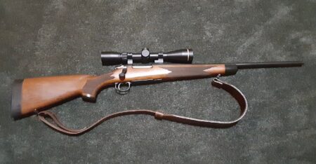 Bolt-action hunting rifle with wooden stock, scope, and brown leather sling
