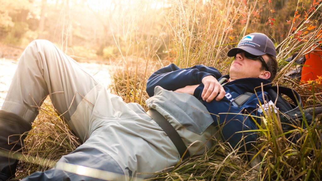 Angler in fly fishing waders napping on shore