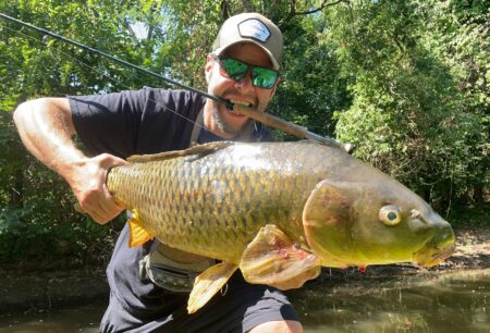 Smiling fisherman holding large common carp caught with fly rod near river