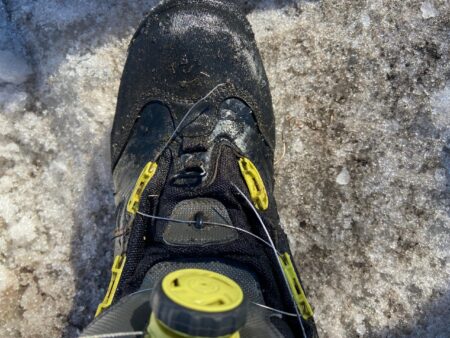 Black mountaineering boot with yellow Boa lacing system standing on snow and ice
