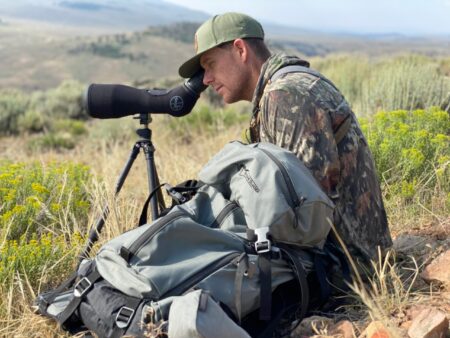 The Best Spotting Scopes Under $1000 (2024 Guide) Hunter in camouflage using Leupold spotting scope on tripod in wilderness landscape.