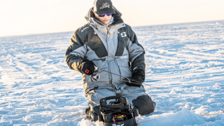 Man in winter gear ice fishing on frozen lake with fishing rod.