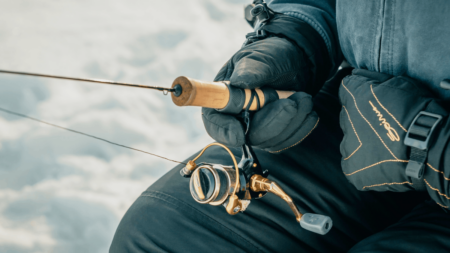 Person in winter gear holding fishing rod with gold spinning reel outdoors.