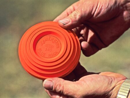 Hands holding a Remington Blue Rock orange clay pigeon shooting target disc