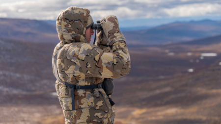 The 6 Best Hunting Jackets of 2024, Expert Tested Person in camouflage gear using binoculars on a mountainous landscape overlook.