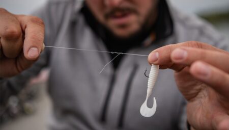 Man tying fishing line to hook with white soft plastic lure bait