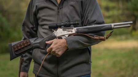 The Ruger-Made Marlin 1895 Trapper is A Lot Like the Old One—Only Better Person holding lever-action rifle with scope and leather sling outdoors.