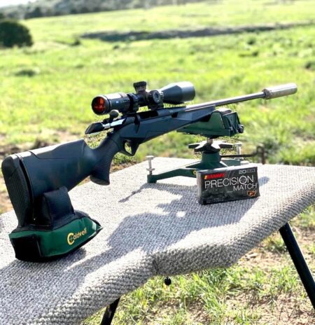 Bolt-action rifle with scope on shooting rest beside Barnes Precision Match ammunition box outdoors