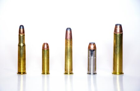 Five brass ammunition cartridges of varying sizes lined up against white background