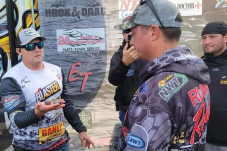 Fishing tournament competitors in sponsor jerseys discuss strategy at outdoor event