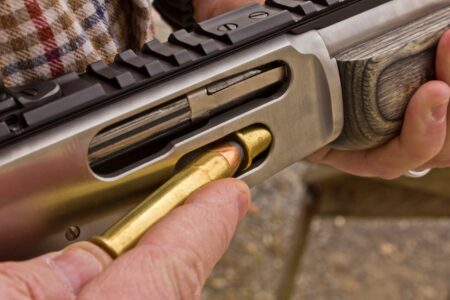 Person loading a rifle cartridge into the chamber of a bolt-action firearm.