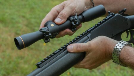Person mounting a rifle scope onto a lever-action rifle outdoors.