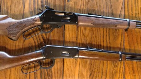 Two lever-action rifles with wooden stocks displayed on hardwood floor side by side.