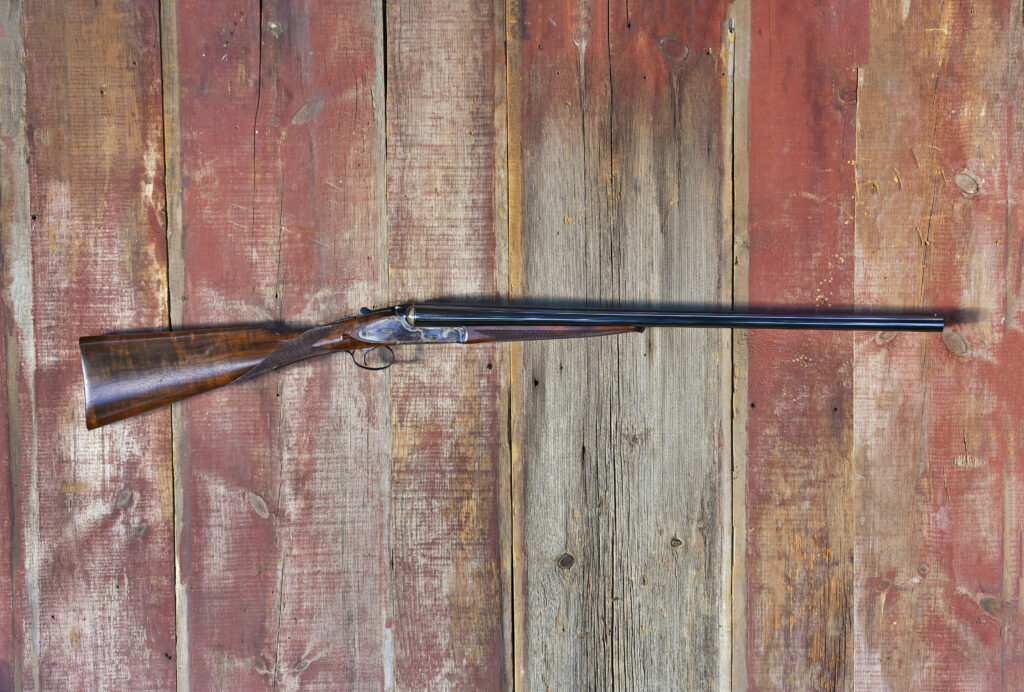 Antique double-barrel shotgun displayed against rustic weathered red wooden barn wall.