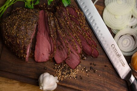 How to Make Venison Pastrami Sliced pastrami on cutting board with Cutluxe knife, garlic, onions, and peppercorns