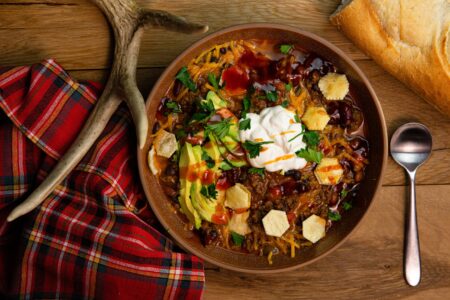 How to Make the Best Venison Chili You’ve Ever Had Hearty beef chili bowl topped with avocado, sour cream, cheese, and hot sauce.