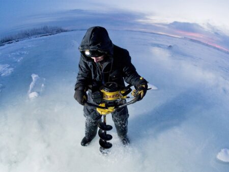 Person using power ice auger drill to bore hole through frozen lake surface