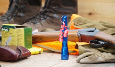 Blue Maglite flashlight gift with red bow surrounded by hunting gear and shotgun