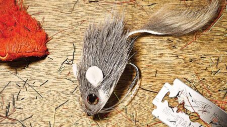 Realistic mouse-shaped fishing fly lure with gray fur and large hook on wood