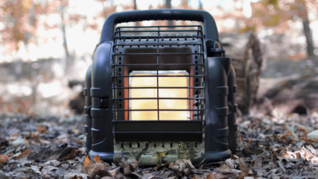 This Portable Heater Has Kept Me Warm On the Coldest Hunts Portable propane Mr. Heater Buddy glowing orange in autumn forest setting outdoors.