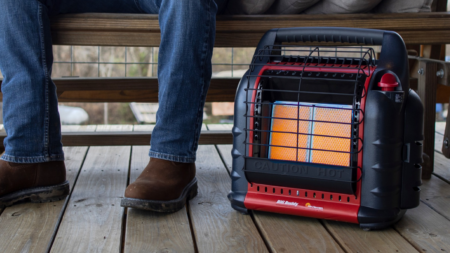 Person sitting near a Mr. Heater Big Buddy portable propane heater on wooden deck.