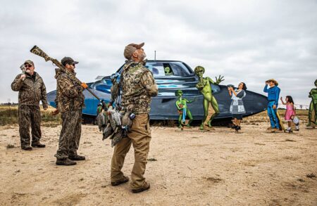 Hunters in camouflage gear stand near a colorful UFO alien roadside attraction display.