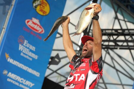 Excited angler holds up two large bass fish at professional fishing tournament