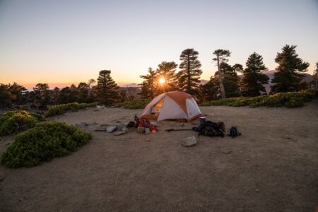 Best Portable Toilets for Camping, Boating, and RV Use Orange camping tent at sunset surrounded by pine trees on rocky mountain terrain.