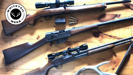 Three hunting rifles displayed on wooden surface with ammunition and deer antler, Whitetail Week