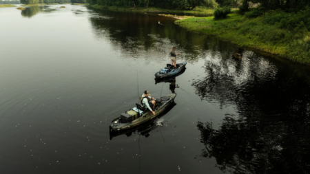 Two anglers fishing from kayaks on a calm river surrounded by lush greenery.