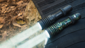 Three Olight tactical flashlights illuminated on black MOLLE gear outdoors.