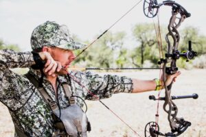 Hunter in camouflage aiming compound bow outdoors in natural wilderness setting