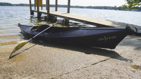 Does a Foldable Kayak Actually Work? I Tried One to Find Out Black Oru Kayak with paddle resting on shoreline beside wooden dock