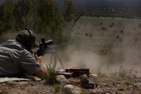 What the Hell is Parallax, and Do Hunters Need to Care About it? Person in prone position firing scoped rifle outdoors in arid desert landscape.