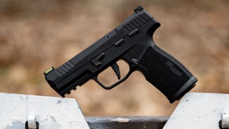 Black SIG Sauer semi-automatic pistol resting on weathered concrete surface outdoors.