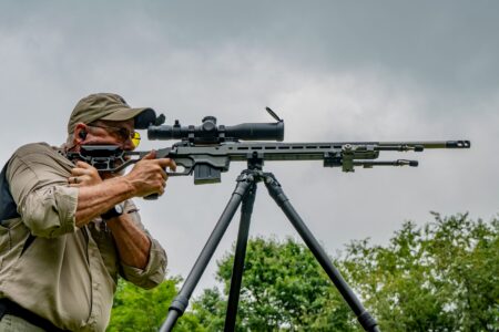 The Long Game: How External Ballistics Influences Bullet Flight Man aiming precision sniper rifle mounted on tripod at outdoor shooting range