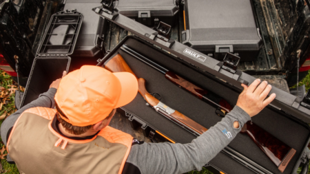 Hunter in orange vest placing rifle into Pelican Vault gun case in truck bed