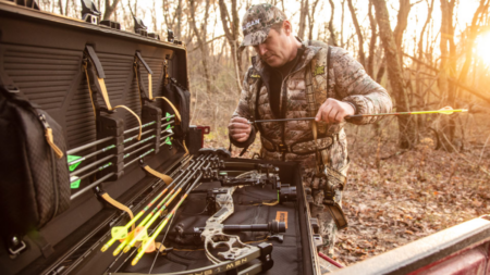 Hunter in camo gear organizing compound bow and arrows from equipment case outdoors.