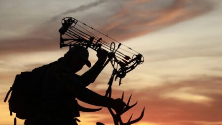 Bowhunter silhouette holding compound bow and deer antlers at sunset