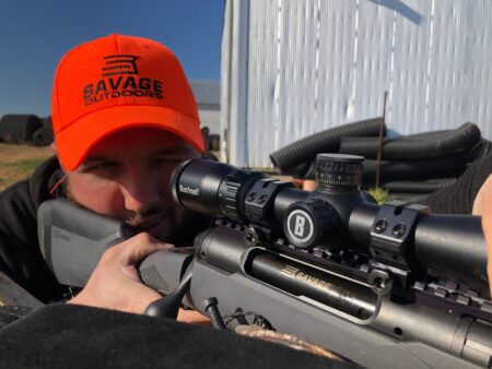 Best 20-Gauge Slug Guns for Deer Hunter aiming Savage rifle with Bushnell scope wearing orange safety cap outdoors