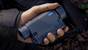 Hand holding a dark blue Pulsar Axion XQ35 Pro thermal monocular outdoors.